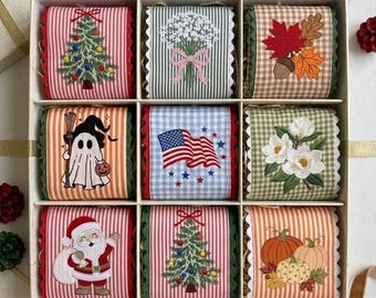 Peut inclure: Un ensemble de neuf ornements en tissu carrés disposés dans une boîte à grille. Les motifs incluent un sapin de Noël, un bouquet floral, des feuilles d'automne, un fantôme, un drapeau américain, des fleurs blanches, le Père Noël et des citrouilles.