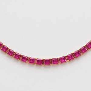 May include: A gold necklace featuring a series of square-cut, vibrant pink gemstones. The gemstones are set closely together, creating a continuous line of color. The necklace is displayed against a plain white background.