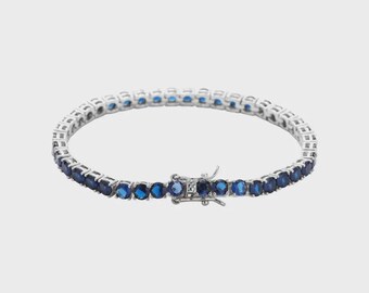 May include: A silver-toned tennis bracelet featuring a row of oval-cut, deep blue gemstones. The bracelet has a secure clasp closure and is displayed against a plain white background. This elegant piece of jewelry is suitable for various occasions.