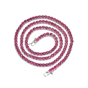 May include: A tennis necklace featuring a continuous strand of vibrant, round, ruby-colored gemstones. The necklace has a silver-colored metal setting and a secure clasp. The gemstones are closely set, creating a seamless, sparkling appearance.