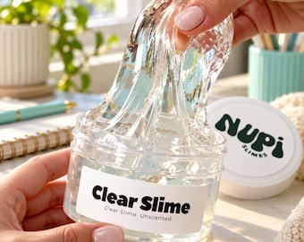 May include: A clear, viscous slime substance being pulled upward from a transparent plastic jar. The jar features a white label with the black text "Clear Slime" and "Clear Slime. Unscented." A separate white lid displays the logo "Nupi Slimes."