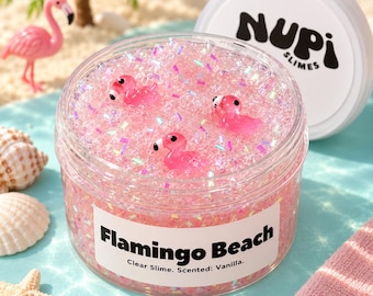 May include: A clear plastic jar filled with pink slime containing iridescent glitter and three small pink flamingo charms. The white label reads Flamingo Beach, Clear Slime, Scented: Vanilla. The lid features the black text NUPI SLIMES.
