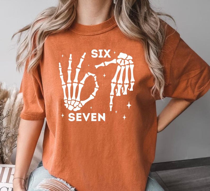 An orange t-shirt with a graphic design featuring skeletal hands and the text "SIX SEVEN" printed on it.