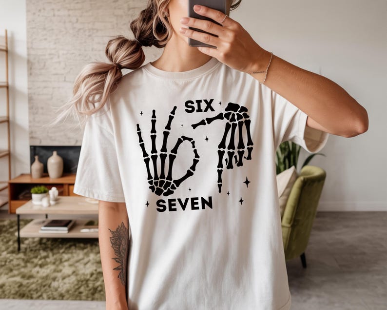 A person wearing a white t-shirt with a graphic design featuring skeletal hands and the text "SIX SEVEN" printed on it.