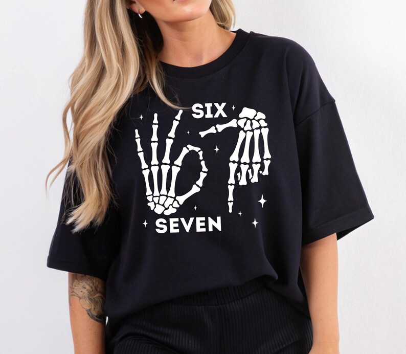 A woman wearing a black t-shirt with a graphic design featuring skeletal hands and the text "SIX SEVEN" printed on it.