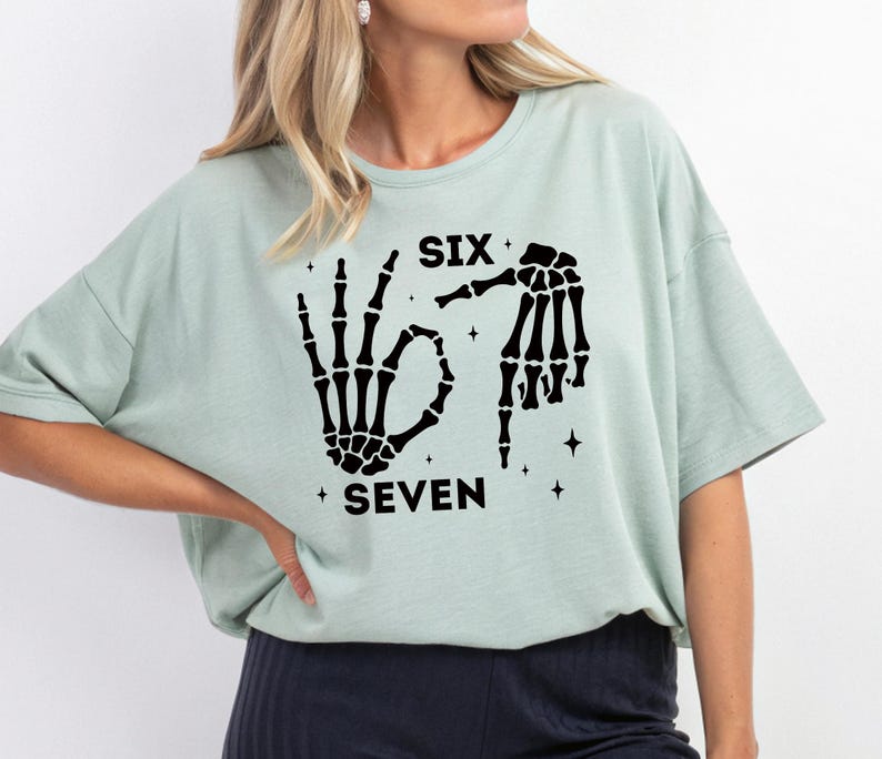 A woman wearing a light green t-shirt with a graphic design featuring a skeleton hand and the text "SIX SEVEN" printed on it.