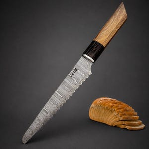 May include: A serrated knife with a Damascus steel blade featuring a wavy pattern and the text JAYGER engraved on the metal. The handle is constructed from two distinct sections of wood, one dark and one light, with a metallic bolster in between.