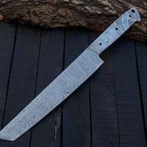 May include: A Damascus steel chef's knife with a wavy pattern blade. The knife has a full tang construction and a pointed tip. The handle area has three holes. The knife is lying on a dark wooden surface.