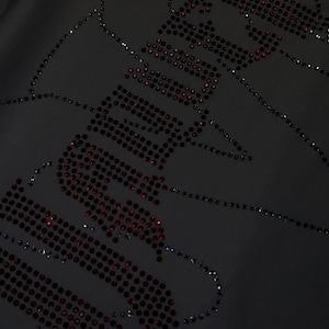 May include: A black fabric garment featuring a decorative design composed of small, dark red rhinestones. The rhinestones are arranged to form the word "SADBOYS" in a stylized, bold font, with additional scattered rhinestone accents.