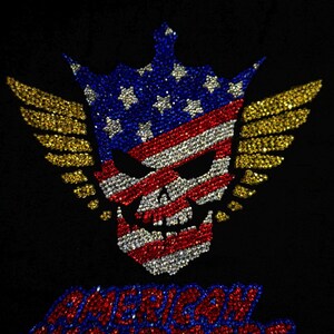 May include: A black garment featuring a rhinestone design of a skull wearing a crown, decorated with the American flag pattern and gold wings. Below the skull, the text AMERICAN NIGHTMARE is spelled out in red and blue rhinestones.