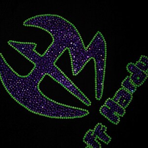 May include: A black garment featuring a large, stylized logo and the text Jeff Hardy. The design is created with purple rhinestones filled in the center and outlined with bright lime green rhinestones, creating a high-contrast, sparkling effect.