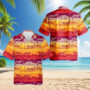 May include: Short-sleeved button-down shirt with a desert-themed pattern. The design features a sunset color scheme with layers of orange, yellow, and red, and silhouettes of coyotes, cacti, and mountains. The shirt is displayed on a beach setting.