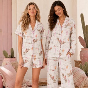 Può includere: Due set di pigiama con una stampa a tema desertico che raffigura cowboy a cavallo e cactus in tonalità rosa e arancione su sfondo crema. Un set include una camicia a maniche corte e pantaloncini, l'altro una camicia a maniche lunghe e pantaloni.