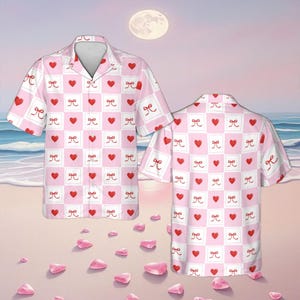 May include: Two short-sleeved button-down shirts with a pink and white checkered pattern. Each square features a red heart or a white bow. The shirts are on a beach with pink petals and a full moon in the background.