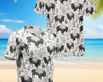 Peut inclure: Deux chemises à manches courtes boutonnées avec un motif répété de bisons et de cactus noirs et blancs sur un fond blanc cassé. Les chemises ont un col classique et sont présentées sur une plage.