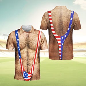 Puede incluir: Camiseta polo de manga corta con un estampado realista de un pecho y torso peludos. La camiseta presenta tirantes al estilo de los tirantes con los colores de la bandera americana, con estrellas y rayas.