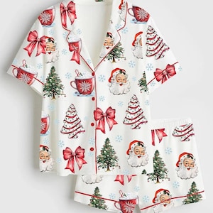 Può includere: Un set di pigiama bianco a maniche corte composto da un top abbottonato e pantaloncini coordinati. Il tessuto presenta una stampa natalizia ripetuta con volti di Babbo Natale, alberi decorati, fiocchi rossi, tazze di cioccolata calda e fiocchi di neve blu.