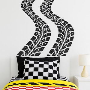 May include: A bedroom with a racing theme. Black tire track decals adorn the white wall above the bed. The bed features a black and white checkered pillow, a yellow stripe, and a red and black checkered comforter.