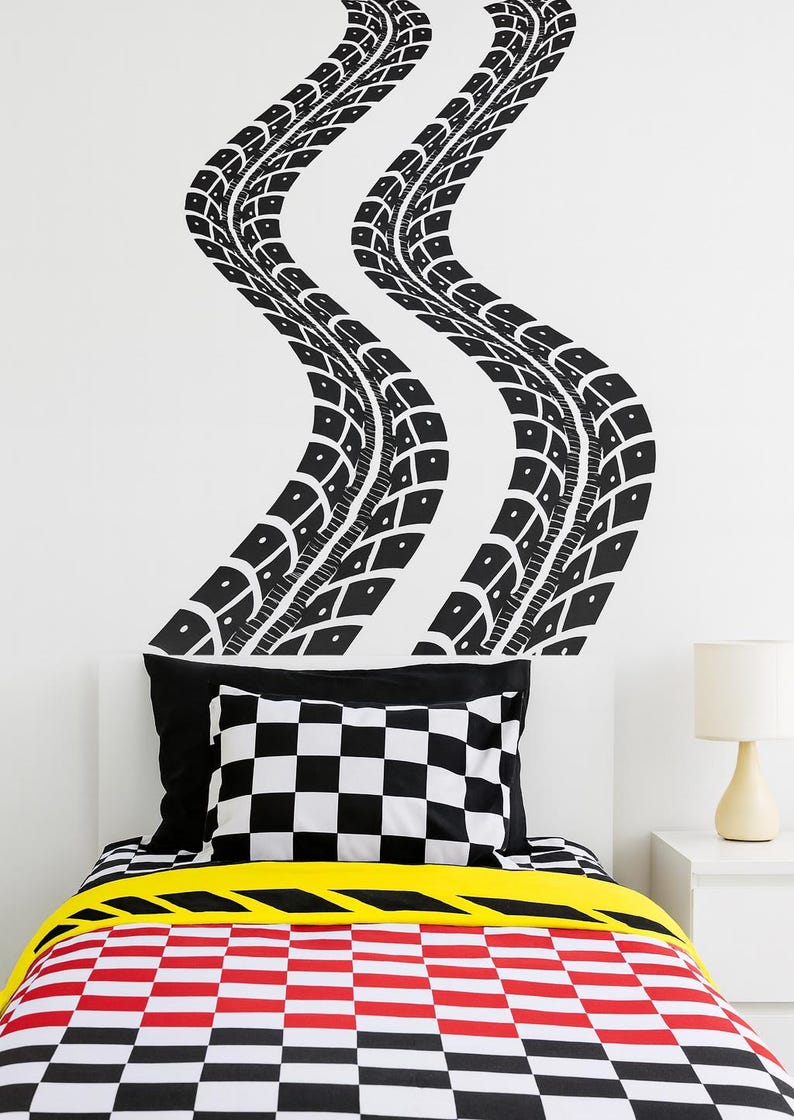 May include: A bedroom with a racing theme. Black tire track decals adorn the white wall above the bed. The bed features a black and white checkered pillow, a yellow stripe, and a red and black checkered comforter.