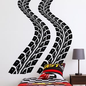 May include: Black tire track wall decals above a bed with a race car theme. The bedding features a checkered pattern and the word "FAST". A pillow and a red car-shaped pillow are on the bed.