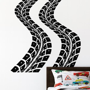 May include: Black tire track wall decals in a wavy pattern. The decals are applied to a white wall above a bed with a race car themed comforter and pillow. The tire tracks add a sporty touch to the room.