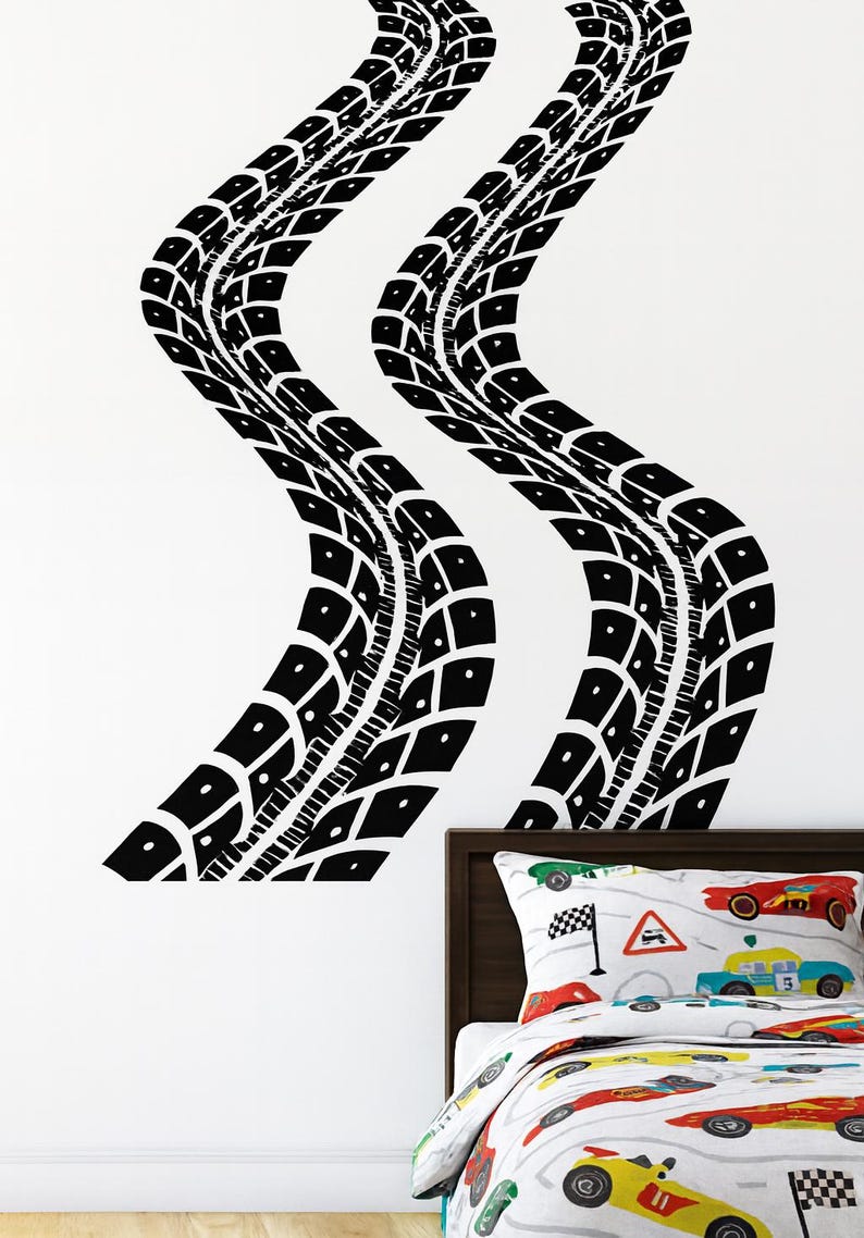 May include: Black tire track wall decals in a wavy pattern. The decals are applied to a white wall above a bed with a race car themed comforter and pillow. The tire tracks add a sporty touch to the room.