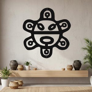 May include: Black metal wall art featuring a stylized sun design with a central face-like shape and radiating petal-like elements. The artwork is mounted on a light-colored wall, creating a striking contrast. Decorative home decor.