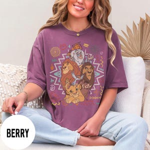 Puede incluir: Camiseta de color bayas con un gr&aacute;fico de personajes de El Rey Le&oacute;n. El dise&ntilde;o incluye a Simba, Mufasa, Tim&oacute;n, Pumba y Zaz&uacute;, rodeados de patrones geom&eacute;tricos coloridos. La camiseta tiene mangas cortas y un corte holgado.