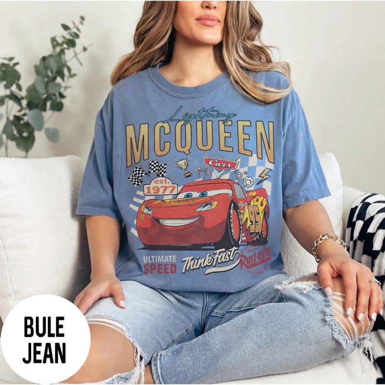 Op de afbeelding: Lichtblauw T-shirt met een afbeelding van Bliksem McQueen uit de film Cars. Het ontwerp bevat de tekst "Lightning McQueen" in goud, een rode raceauto en de woorden "Ultimate Speed" en "Think Fast."