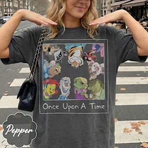 May include: Dark gray t-shirt featuring a framed graphic with cartoon characters and the text "Once Upon A Time." The graphic includes a raccoon, tiger, pig, and other characters. The shirt has a relaxed fit.