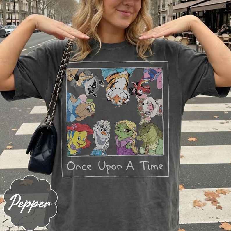 May include: Dark gray t-shirt featuring a framed graphic with cartoon characters and the text "Once Upon A Time." The graphic includes a raccoon, tiger, pig, and other characters. The shirt has a relaxed fit.