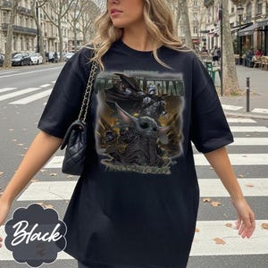 Puede incluir: Una camiseta negra de manga corta con un estampado gr&aacute;fico de The Mandalorian y Grogu. El dise&ntilde;o incluye el texto "STAR WARS THE MANDALORIAN" en la parte superior y "THIS IS THE WAY" en la parte inferior, sobre un fondo oscuro y ahumado.