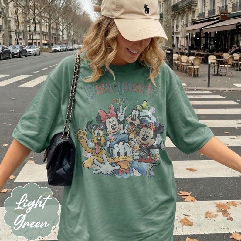 Pu&ograve; includere: T-shirt verde chiaro con grafica Disney World 2026 con Topolino, Minnie, Paperino, Pippo e Pluto. La maglietta &egrave; verde chiaro e ha maniche corte. Le parole "Light Green" sono in un carattere decorativo.