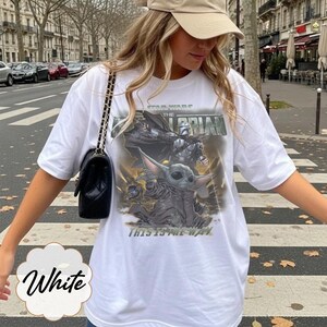 Puede incluir: Una camiseta blanca de manga corta con un estampado gr&aacute;fico de The Mandalorian y Grogu. El dise&ntilde;o incluye el texto Star Wars The Mandalorian y This Is The Way en una fuente desgastada. La camiseta tiene cuello redondo y un corte holgado.