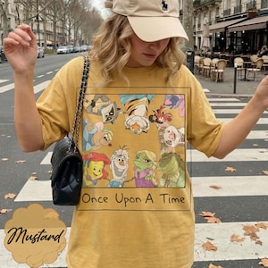 May include: Mustard-colored t-shirt featuring a rectangular graphic with cartoon characters and the text "Once Upon A Time." The shirt has short sleeves and a crew neck. The word "Mustard" is written in a cursive font at the bottom.