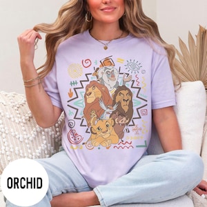 Puede incluir: Camiseta color orqu&iacute;dea con un gr&aacute;fico de personajes de El Rey Le&oacute;n. El dise&ntilde;o incluye a Simba, Mufasa, Tim&oacute;n, Pumba y otros personajes. La camiseta tiene cuello redondo y mangas cortas.