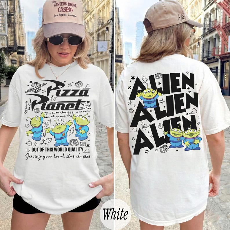 K&ouml;nnte beinhalten: Wei&szlig;es T-Shirt mit einem Pizza Planet-Motiv auf der Vorderseite und Alien-Charakteren auf der R&uuml;ckseite. Das Frontdesign enth&auml;lt den Text "Pizza Planet" und Cartoon-Aliens. Auf der R&uuml;ckseite steht das Wort "ALIEN" wiederholt.
