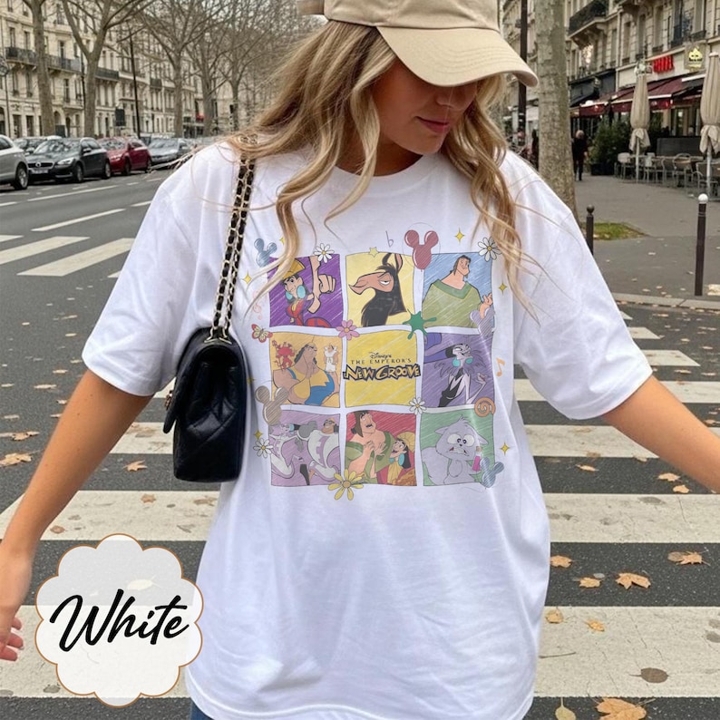 May include: A white short-sleeved t-shirt featuring a grid-style graphic print of characters from The Emperor's New Groove. The design includes various scenes and the movie title in the center, accented with small flower and star illustrations.