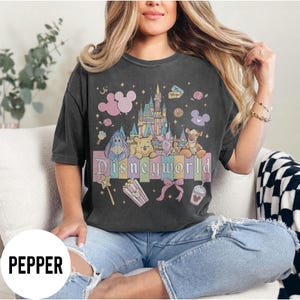 May include: Dark gray t-shirt featuring a colorful Disneyworld graphic. The design includes a castle, various Disney characters, and the word "Disneyworld" in pastel colors. The shirt has a vintage, worn look.
