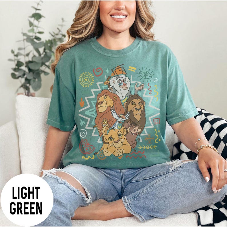 Puede incluir: Camiseta verde claro con un dise&ntilde;o de personajes de El Rey Le&oacute;n. El dise&ntilde;o incluye a Simba, Mufasa, Tim&oacute;n, Pumba y Zaz&uacute;, con patrones coloridos de inspiraci&oacute;n tribal. La camiseta es de corte holgado.