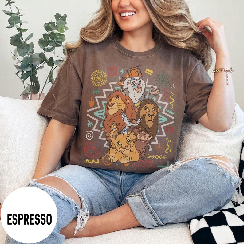 Puede incluir: Camiseta color espresso con un gr&aacute;fico de personajes de El Rey Le&oacute;n. El dise&ntilde;o incluye a Simba, Mufasa y otros personajes, rodeados de coloridos patrones de estilo tribal. La camiseta es de corte holgado.