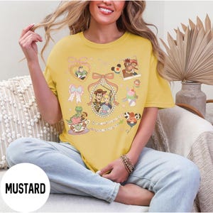 May include: Mustard yellow t-shirt featuring cartoon characters. The shirt has a round neckline and short sleeves. The graphic includes images of Woody, Buzz Lightyear, and other characters. The word "MUSTARD" is printed at the bottom of the image.