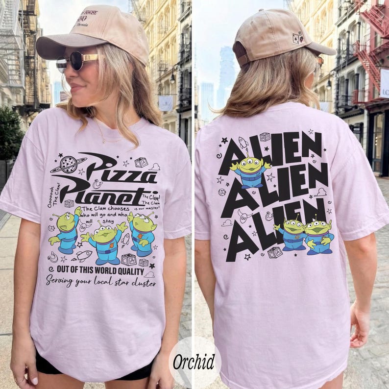 K&ouml;nnte beinhalten: Helllila T-Shirt mit dem Pizza Planet Logo und Alien-Charakteren auf der Vorderseite. Auf der R&uuml;ckseite des Shirts steht das Wort "ALIEN" wiederholt mit Alien-Grafiken. Das Shirt ist kurz&auml;rmlig und hat einen l&auml;ssigen Stil.