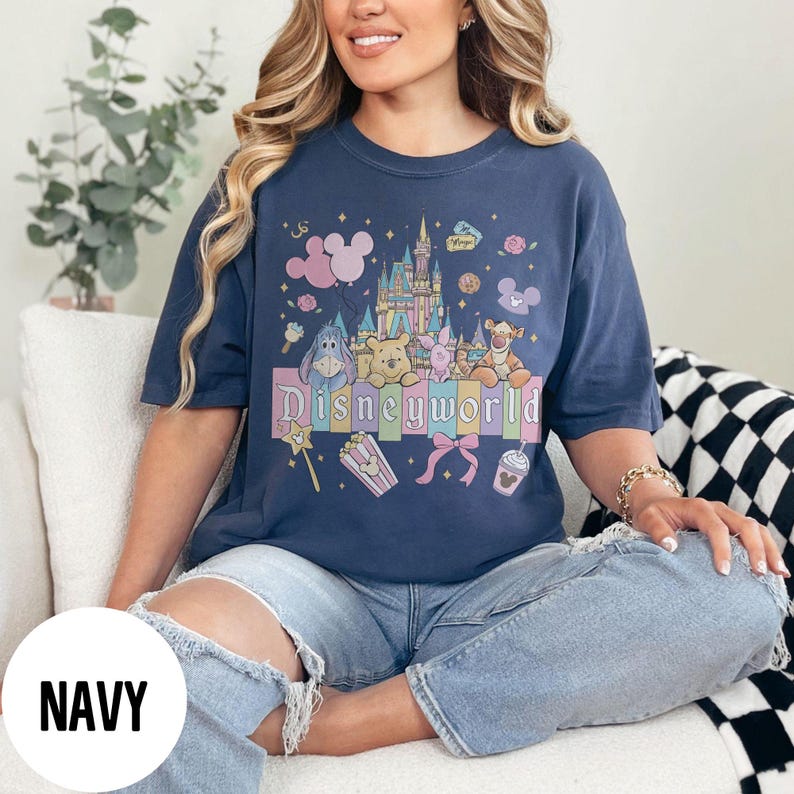 May include: Navy blue t-shirt featuring a colorful Disneyworld graphic. The design includes a castle, balloons, and various Disney characters such as Winnie the Pooh, Piglet, and Tigger. The word "Disneyworld" is prominently displayed.