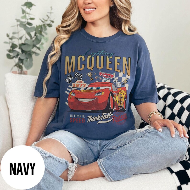 Op de afbeelding: Marineblauw T-shirt met een afbeelding van Bliksem McQueen uit de film Cars. Het ontwerp bevat de tekst "Lightning McQueen", "Cars", "est. 1977" en "Ultimate Speed Think Fast". Het shirt heeft een vintage, distressed look.