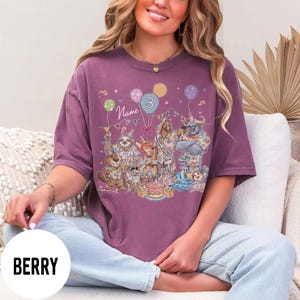 以下が含まれることがあります： ベリー色のTシャツ。漫画の動物、風船、ケーキが登場する、気まぐれな誕生日パーティーのシーンが描かれています。「3」の数字と「Name」の文字も表示されています。ゆったりとした快適なフィット感のシャツです。