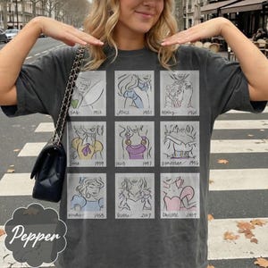 May include: Dark gray t-shirt featuring a grid of nine cartoon sketches of animated characters with their names and years. The word "Pepper" is printed on the bottom left. The shirt is a casual style.