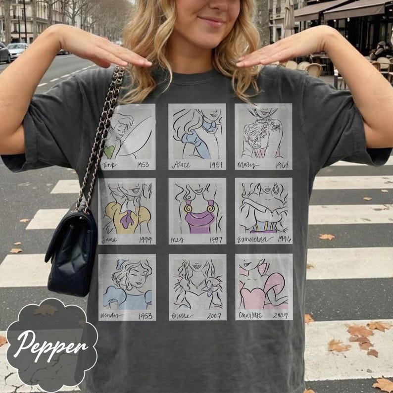 May include: Dark gray t-shirt featuring a grid of nine cartoon sketches of animated characters with their names and years. The word "Pepper" is printed on the bottom left. The shirt is a casual style.