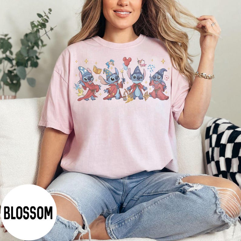 May include: A light pink t-shirt featuring a graphic of four cartoon characters dressed in wizard attire. The characters are in various poses, holding items like books and wands. The word "BLOSSOM" is printed in white at the bottom left.