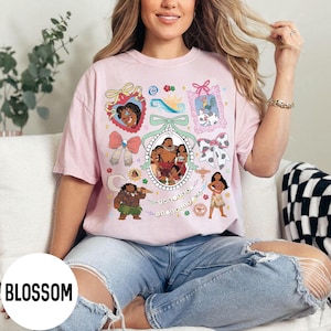 Pu&ograve; includere: T-shirt rosa chiaro con un collage di personaggi dei cartoni animati ed elementi decorativi. Il design include immagini incorniciate, fiocchi e il testo "The Sea Called Me". La maglietta ha una vestibilit&agrave; ampia.